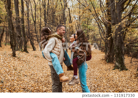 Mother and father kissing while carry daughter on their backs, piggyback ride. 131917330