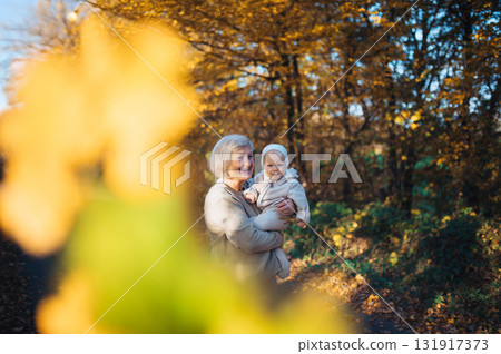 Grandma holding baby in warm embrace during fall season. Grandma holding baby in warm embrace during fall season. 131917373
