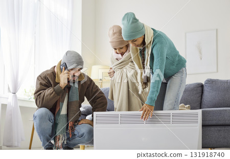 Cold family in scarves and hats relying on electric heater to save energy Cold family in scarves and hats relying on electric heater to save energy 131918740