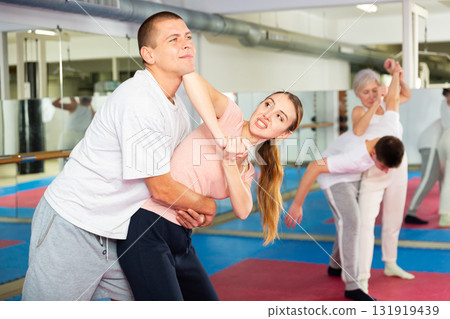 Girl trying to escape rear hug of male opponent, striking with elbow to chin Girl trying to escape rear hug of male opponent, striking with elbow to chin 131919439