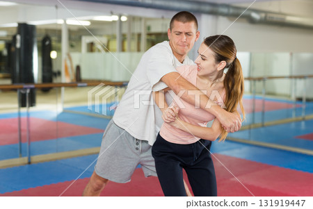 Girl trying to escape rear grab attack striking ribs with elbow during self defense course 131919447