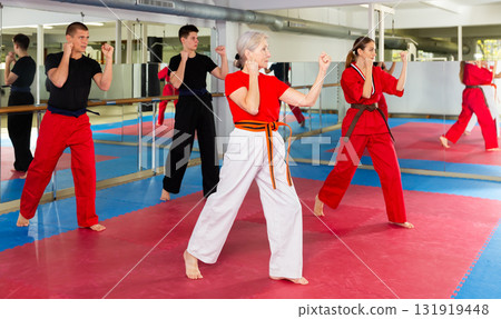 Aged woman practicing martial arts with group in gym Aged woman practicing martial arts with group in gym 131919448