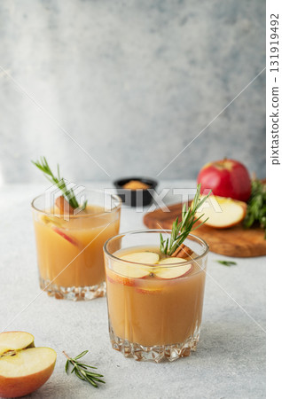 Two glasses of hot apple cider with cinnamon, anise, and rosemary on a light background Two glasses of hot apple cider with cinnamon, anise, and rosemary on a light background 131919492