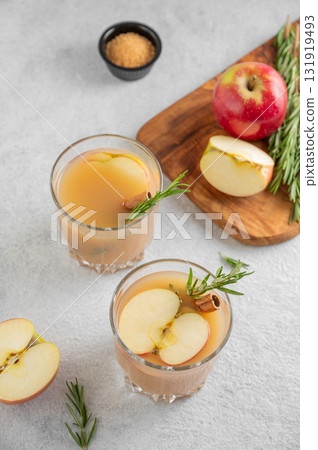 Two glasses of hot apple cider with cinnamon, anise, and rosemary on a light background Two glasses of hot apple cider with cinnamon, anise, and rosemary on a light background 131919493