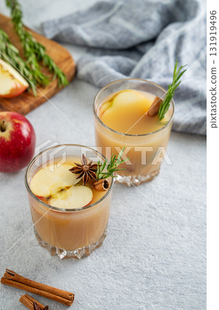 Two glasses of apple cider with cinnamon, anise, and rosemary on a light background with fruits Two glasses of apple cider with cinnamon, anise, and rosemary on a light background with fruits 131919496