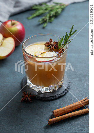 Hot apple cider with cinnamon, anise, and rosemary in glass on a dark blue background with fruits 131919501