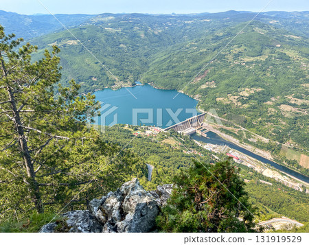 Scenic aerial view of hydroelectric dam on turquoise lake surrounded by lush green forest 131919529