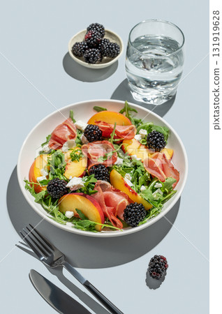 Salad with peaches, arugula, feta, prosciutto and berries in a plate on a blue background 131919628