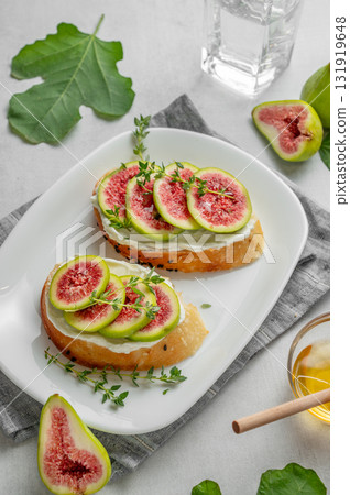 Sweet toasts with fresh figs, cheese, thyme, and honey on a light background. 131919648