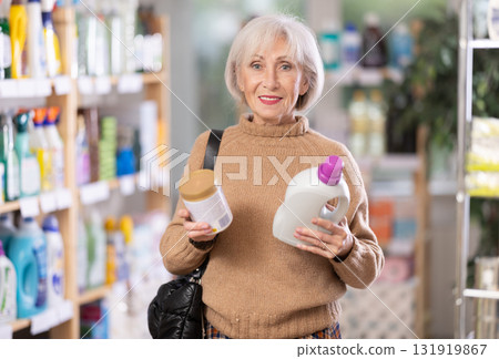 Mature positive woman consumer with household chemical products for washing indoors Mature positive woman consumer with household chemical products for washing indoors 131919867