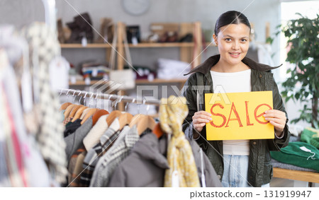 Asian woman holds yellow poster informing about discounts in store Asian woman holds yellow poster informing about discounts in store 131919947