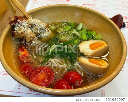 A bowl of ramen with egg, cherry tomatoes and sesame chicken. Asian cuisine, comfort food and dining experience representing balance, flavor and culinary aesthetics. 131920097