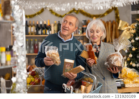 Portrait of elderly couple with sweet products in supermarket - nougat, panettone, marzipan, panellets Portrait of elderly couple with sweet products in supermarket - nougat, panettone, marzipan, panellets 131920109