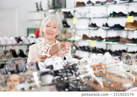 Mature woman who came to shoe store for shopping, chooses summer shoes Mature woman who came to shoe store for shopping, chooses summer shoes 131920174
