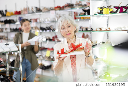 Mature woman who came to shoe store for shopping, chooses summer shoes Mature woman who came to shoe store for shopping, chooses summer shoes 131920195