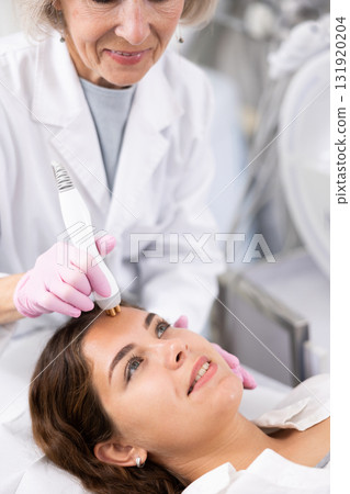 Young woman having face radiolifting procedure made by doctor 131920204