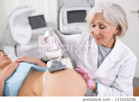 Old woman specialist doing LPG massage of hips of young woman 131920206