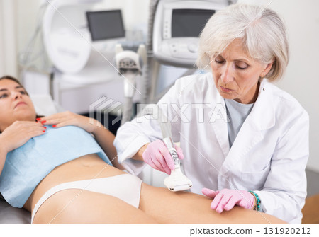 Old woman specialist doing vacuum massage of hips of young woman Old woman specialist doing vacuum massage of hips of young woman 131920212