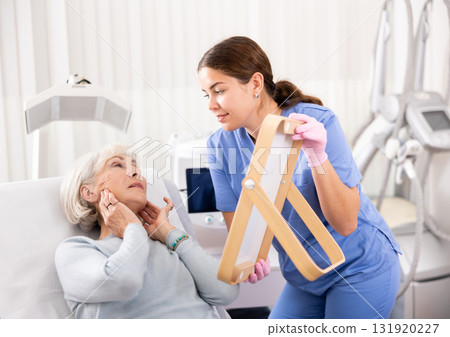 Old woman having consultation about face aesthetic while looking in the mirror 131920227
