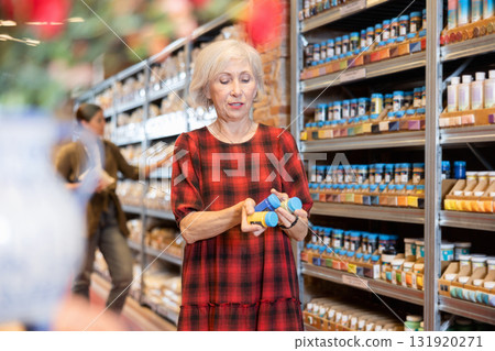 Elderly woman chooses multi-colored pigments for her future clay or ceramic dishes in specialized store 131920271