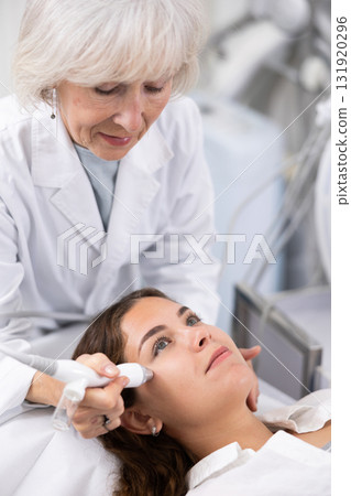 Young woman at appointment with beautician doing ultrasound face cleaning with help of high-frequency ultrasonic waves in cosmetology clinic 131920296