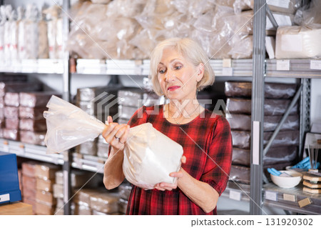Elderly woman chooses pottery clay in shop 131920302