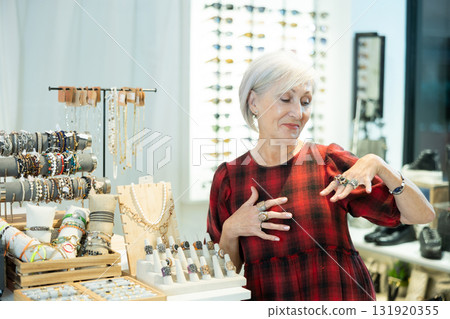 Cheerful elderly woman choosing rings from display with costume jewelry in boutique 131920355