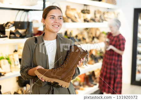 Girl buyer looks at footwear from new collection and picks up new pair of boots for winter. Girl buyer looks at footwear from new collection and picks up new pair of boots for winter. 131920372