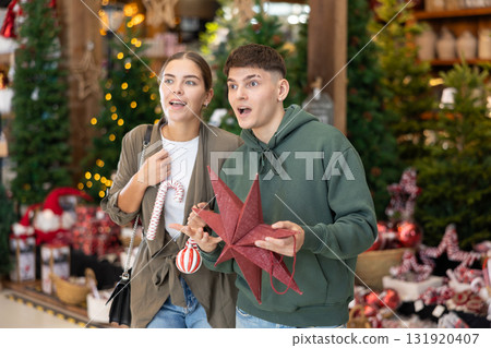 Girl with guy buyer considers New Year and Christmas decorations ornaments for Christmas tree 131920407