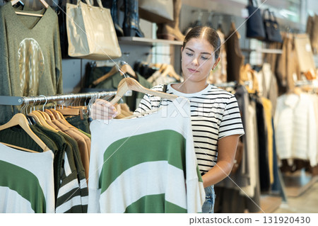 Girl customer in store has removed hanger with jersey from window and is considering product. Girl customer in store has removed hanger with jersey from window and is considering product. 131920430