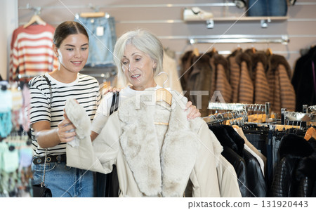Girl consults with senior female friend about quality fur coat during shopping in clothes store 131920443