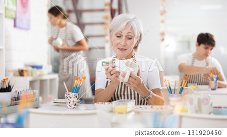 Interested elderly woman painting on ceramic cup during pottery class 131920450