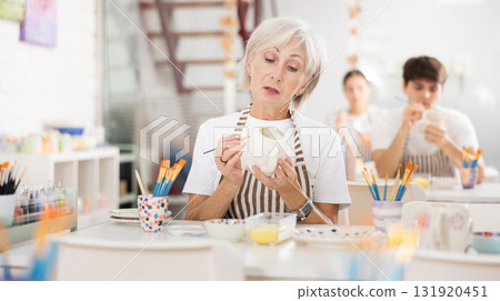 Interested elderly woman painting on ceramic cup during pottery class Interested elderly woman painting on ceramic cup during pottery class 131920451
