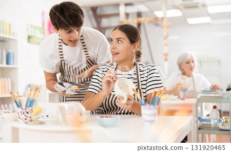 Young craftsman sharing art of ceramics painting with girl in pottery class 131920465