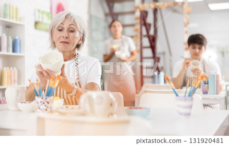 Experienced female artist painting ceramic cup in pottery workshop Experienced female artist painting ceramic cup in pottery workshop 131920481