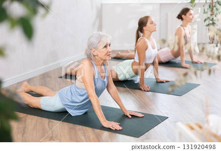 Women three generations practicing yoga positions during group training in fitness center, performing stretching asana Urdhva Mukha Shvanasana in studio Women three generations practicing yoga positions during group training in fitness center, performing stretching asana Urdhva Mukha Shvanasana in studio 131920498