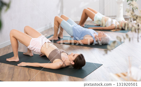 Young woman doing Setu Bandha Sarvangasana during group yoga training Young woman doing Setu Bandha Sarvangasana during group yoga training 131920501
