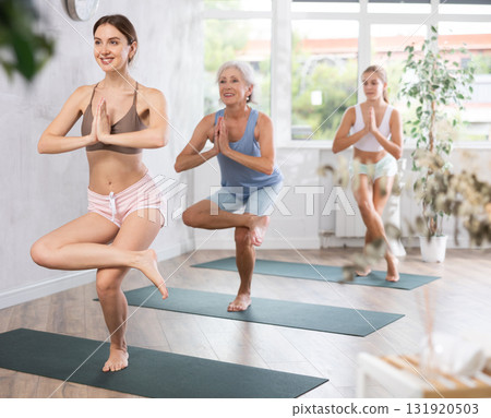 Three generations of women perform lightweight variation of garudanasan eagle pose in gym 131920503