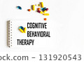 The text "COGNITIVE BEHAVIORAL THERAPY" is written in a notebook next to pills. Medical concept 131920543