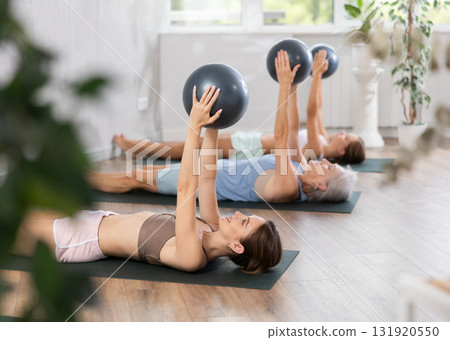Women different ages maintaining physical health practicing pilates with soft balls at group workout Women different ages maintaining physical health practicing pilates with soft balls at group workout 131920550