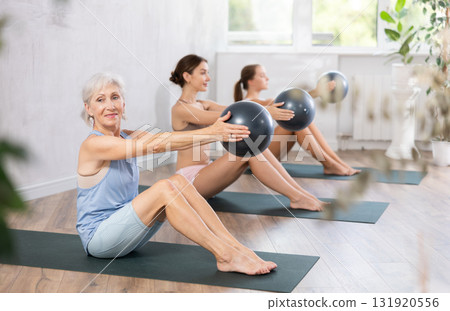 Elderly woman doing pilates with soft ball in group Elderly woman doing pilates with soft ball in group 131920556