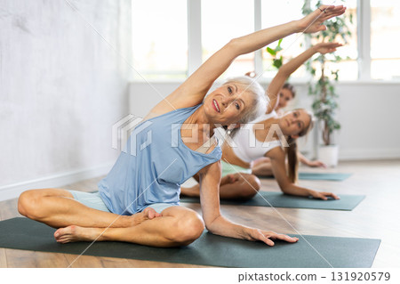 Active women three generations exercising during yoga class in fitness center, vakrasana pose Active women three generations exercising during yoga class in fitness center, vakrasana pose 131920579