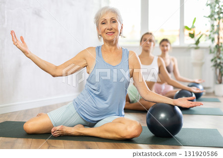 Family grandmother, mother and granddaughter perform fitness exercise sitting on floor with softball 131920586