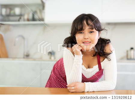 Positive woman in apron standing at kitchen interior near countertop 131920612
