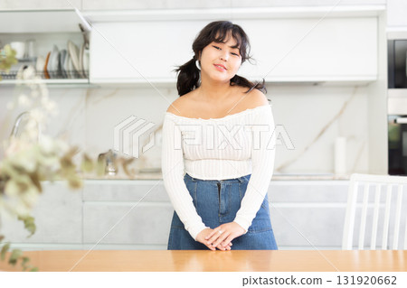 Portrait of young housewife in white blouse and denim skirt standing in kitchen, posing on camera 131920662