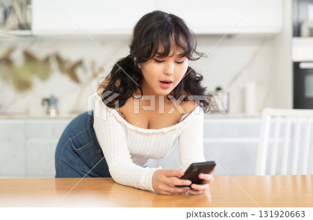 Smiling girl texting on her smartphone at living room Smiling girl texting on her smartphone at living room 131920663