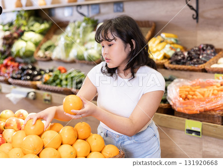Attentive young woman purchaser choosing oranges in grocery store Attentive young woman purchaser choosing oranges in grocery store 131920668