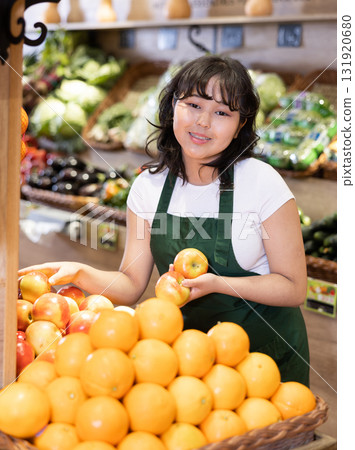 Young saleswoman placing oranges on food stall in grocery store Young saleswoman placing oranges on food stall in grocery store 131920680