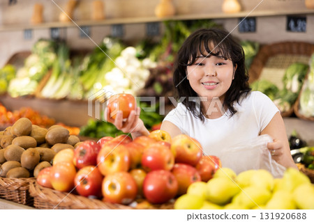 Delighted young woman purchaser choosing apples in grocery store 131920688