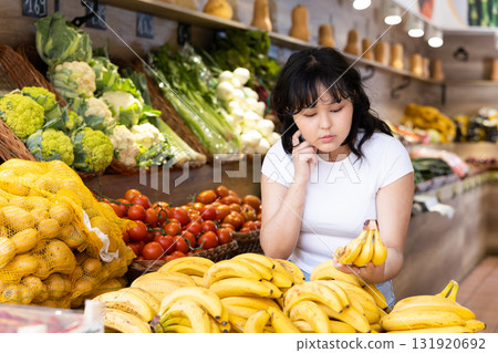 Young girl choosing fresh bananas in fruit and vegetable section of supermarket Young girl choosing fresh bananas in fruit and vegetable section of supermarket 131920692